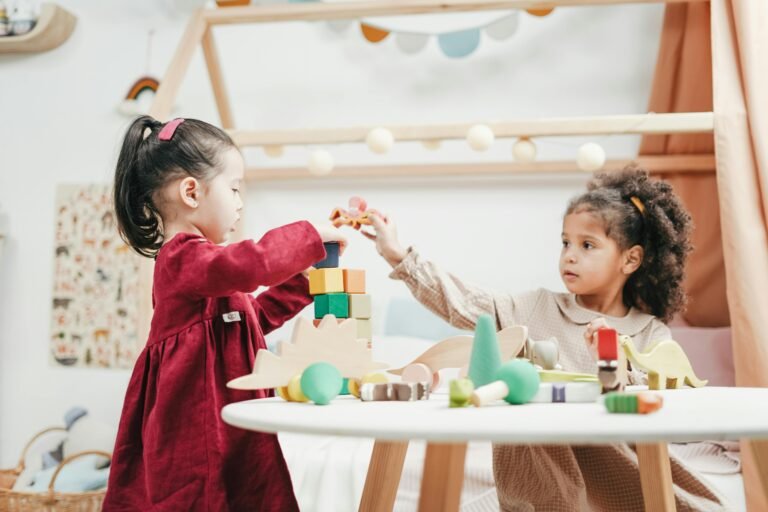 Two preschool-aged children playing with blocks and toys at a round table.